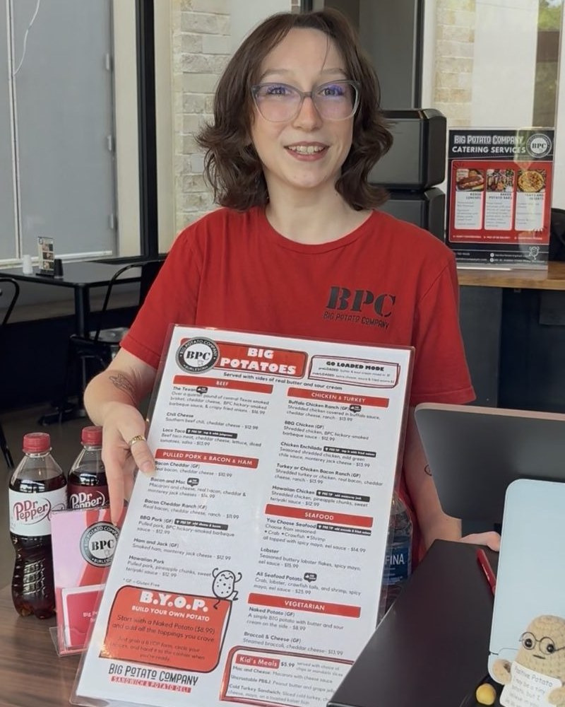 A Big Potato Company team member at the front counter, holding out the Big Potatoes menu